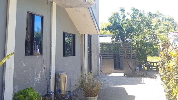 A residential building with a concrete facade, a water tank on the roof, and a paved driveway.