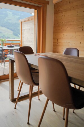 Ein Essbereich mit Holztisch und -stühlen, Blick ins Freie und einer Holzwand.