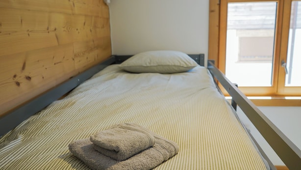 A single bed with a striped bedspread, a pillow, and two folded towels. - New Apartment in the Heart of Arêches · With Balcony & Private Parking (Beaufort)