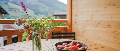 Une table ornée d’un vase de fleurs et d’un saladier de fruits, placée sur un balcon offrant une vue sur la montagne.