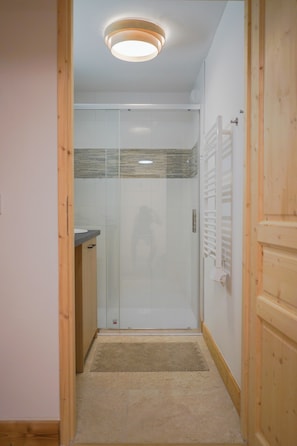 A bathroom with a glass shower enclosure, a wooden door, and a white tiled wall. - New Apartment in the Heart of Arêches · With Balcony & Private Parking (Beaufort)