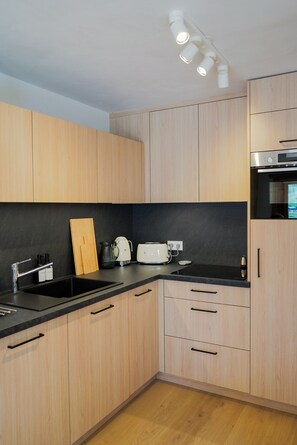 A modern kitchen with wooden cabinets, a black countertop, a sink, a toaster, and a kettle. - New Apartment in the Heart of Arêches · With Balcony & Private Parking (Beaufort)