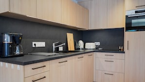 A modern kitchen with light wood cabinets, a black countertop, a coffee maker, a kettle, and a toaster. - New Apartment in the Heart of Arêches · With Balcony & Private Parking (Beaufort)