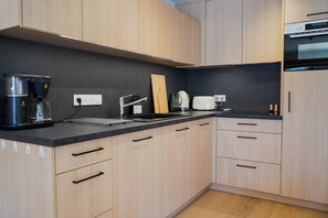 Eine moderne Küche mit hellen Holzschränken, einer schwarzen Arbeitsplatte, einer Kaffeemaschine, einem Wasserkocher und einem Toaster.