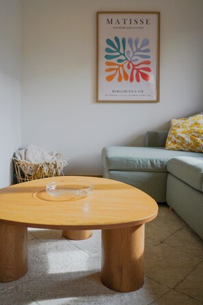 Ein Wohnzimmer mit einem Holztisch, einem gerahmten Kunstwerk an der Wand, einem Sofa und einem dekorativen Kissen.