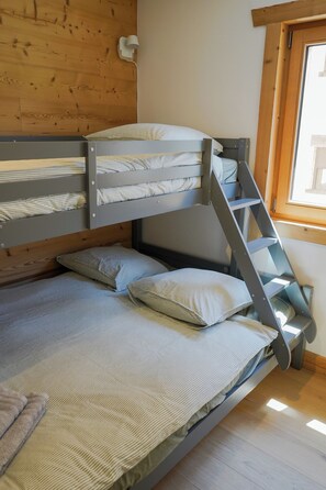 A bunk bed with striped bedding and pillows, wooden walls, a window, and a light switch on the wall. - New Apartment in the Heart of Arêches · With Balcony & Private Parking (Beaufort)