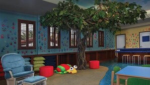 Une salle de jeux pour enfants avec un arbre, des empreintes de mains colorées sur les murs et un tapis bleu.