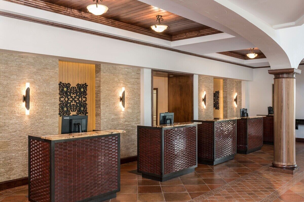 A reception area with a modern design, featuring a reception desk, a wall-mounted light fixture, and a wooden column.