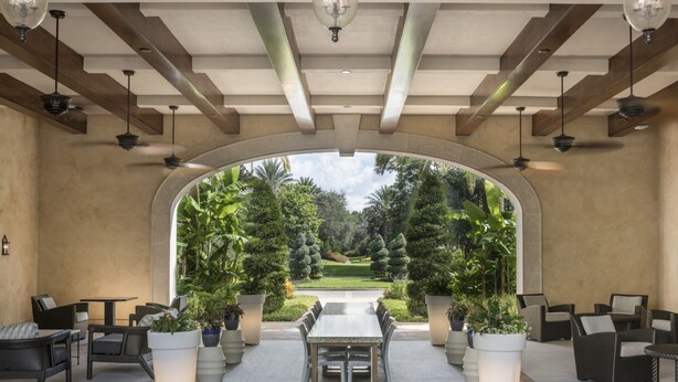 An outdoor patio with a dining table and chairs, surrounded by potted plants and a view of a well-manicured garden.