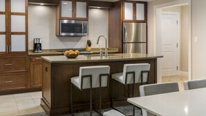 A modern kitchen with a central island, bar stools, stainless steel appliances, and wooden cabinetry.