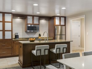 A modern kitchen with a central island, bar stools, stainless steel appliances, and wooden cabinetry. - 3 Bedroom Villa at Lakeshore Reserve w/ Amenities (Orlando)