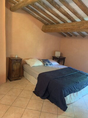 Ein Schlafzimmer mit einem Bett, einem Nachttisch, einem Schrank und einer schrägen Decke mit Holzbalken.