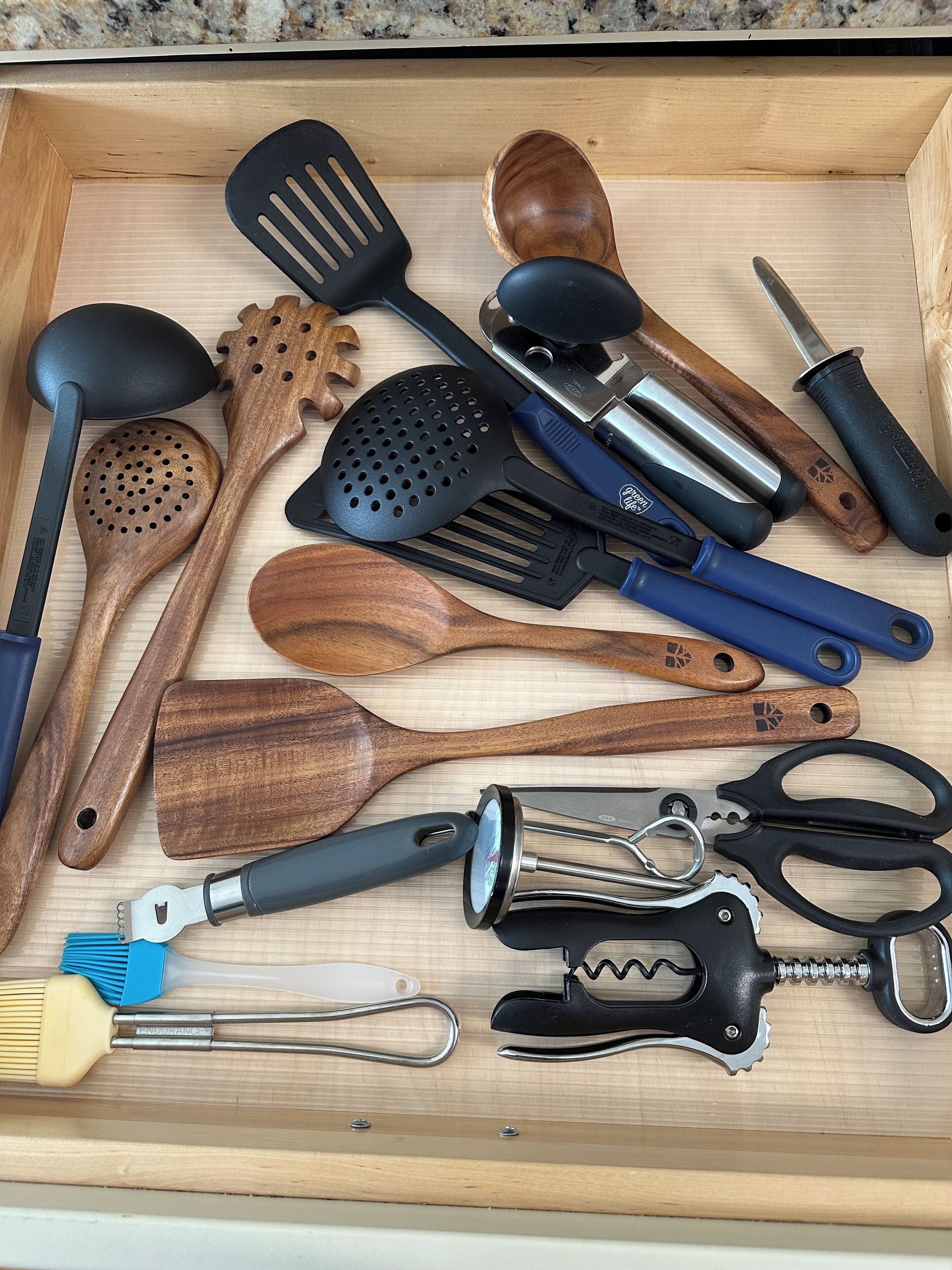 A drawer containing various kitchen utensils including wooden spoons, spatulas, and a bottle opener.