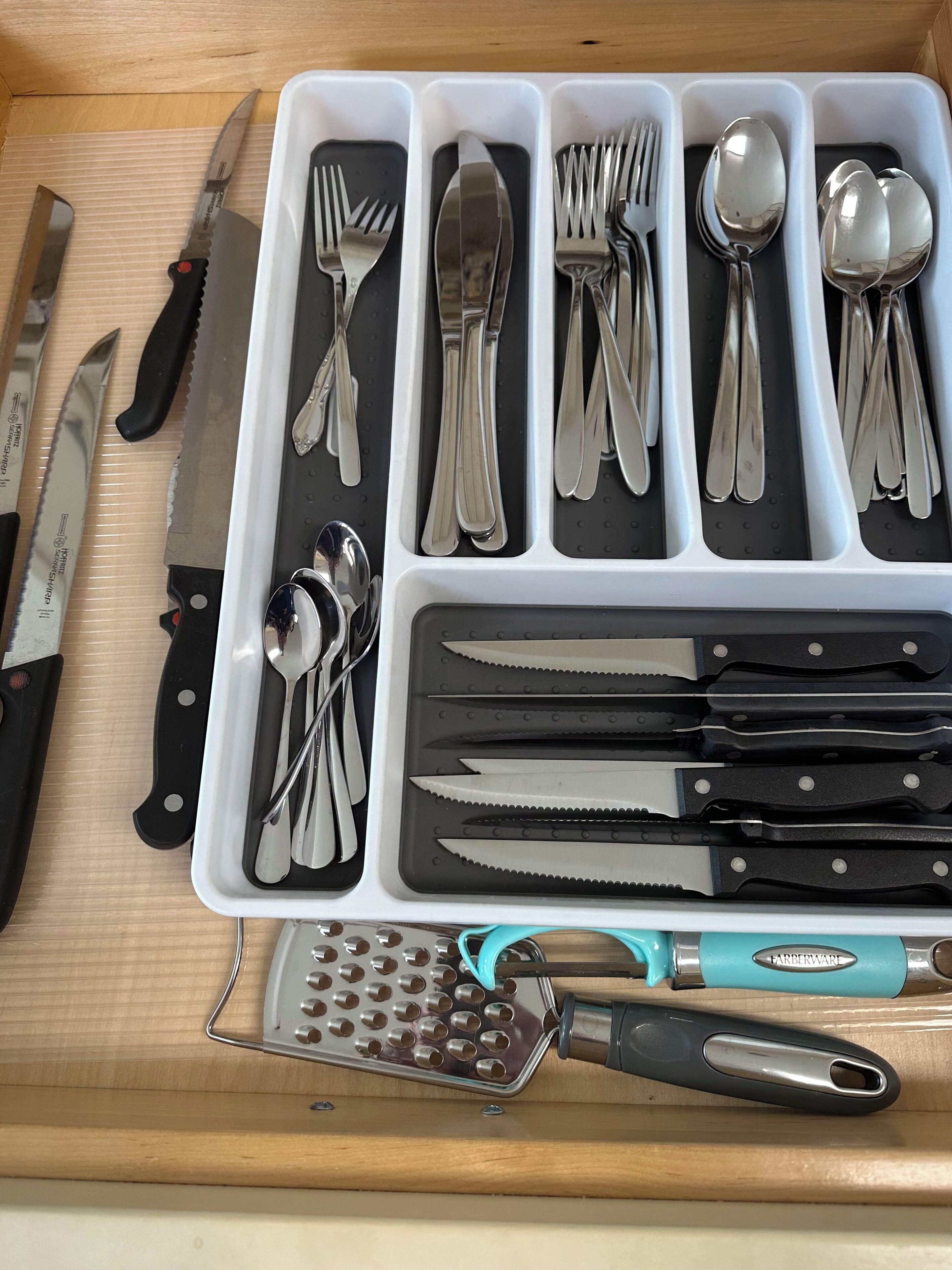 A drawer with compartments containing various kitchen utensils and a grater.