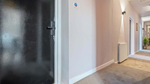 En gang med en sort dør, en hvid væg med et blåt skilt, og en radiator til højre.