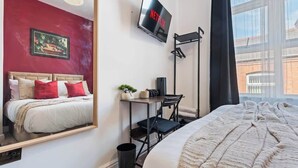 Et hotelværelse med en seng, et skrivebord med stol, et TV ophængt på væggen og et vindue med udsigt til bygninger.