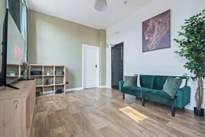 A living room with a green sofa, wooden flooring, a white door, and a plant. - Central Studio with Double Bed | CV2 |Free Parking (Coventry)