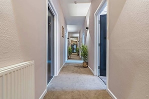 A hallway with a carpeted floor, white walls, and doors on both sides. - Central Studio with Double Bed | CV2 |Free Parking (Coventry)