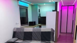 A modern room with a sofa, a kitchen area, and a hallway with a door. - The Albino Oracle (Nîmes)