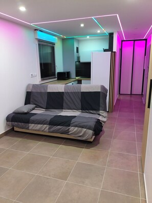 A modern room with a sofa, a kitchen area, and a hallway with a door. - The Albino Oracle (Nîmes)