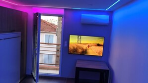 A room with a large flat-screen TV mounted on the wall, a bench, and a sliding door leading to an outdoor area. - The Albino Oracle (Nîmes)