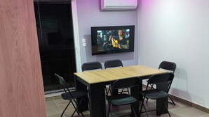 A room with a wooden table and four chairs, a television mounted on the wall, and a bed in the foreground. - The Albino Oracle (Nîmes)