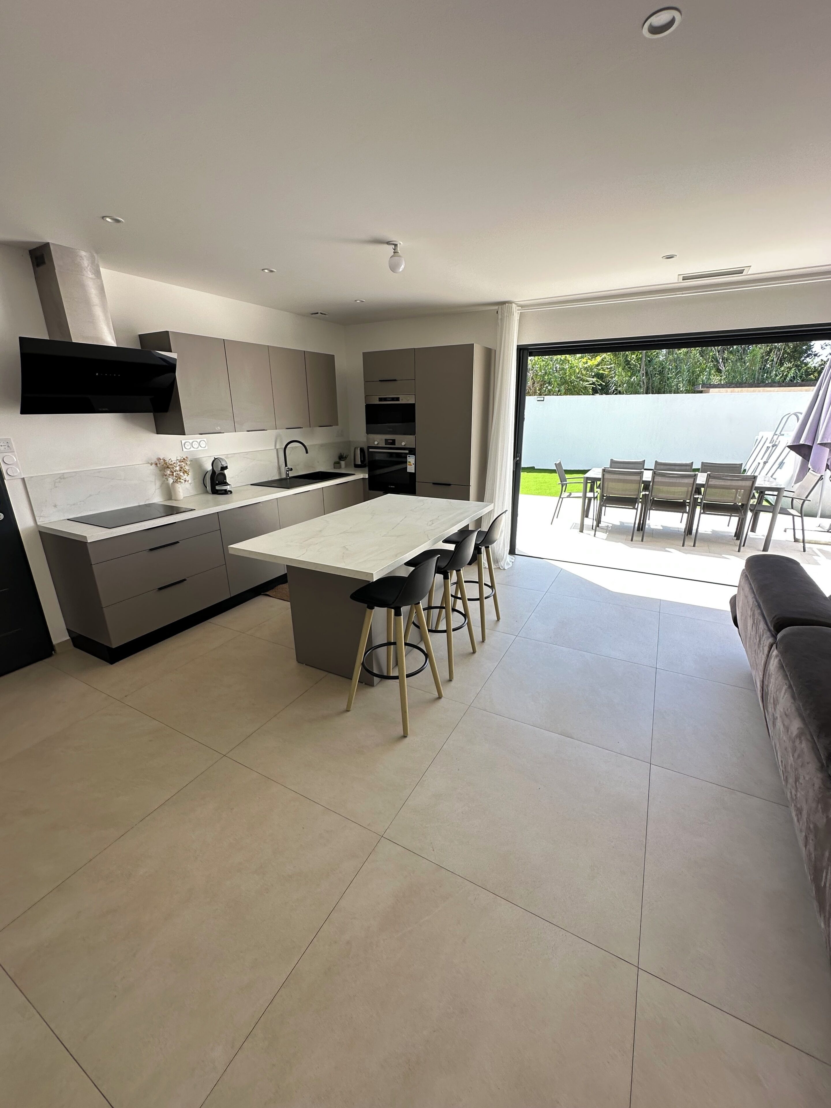 A modern kitchen with a central island, built-in appliances, and a dining area with outdoor seating.