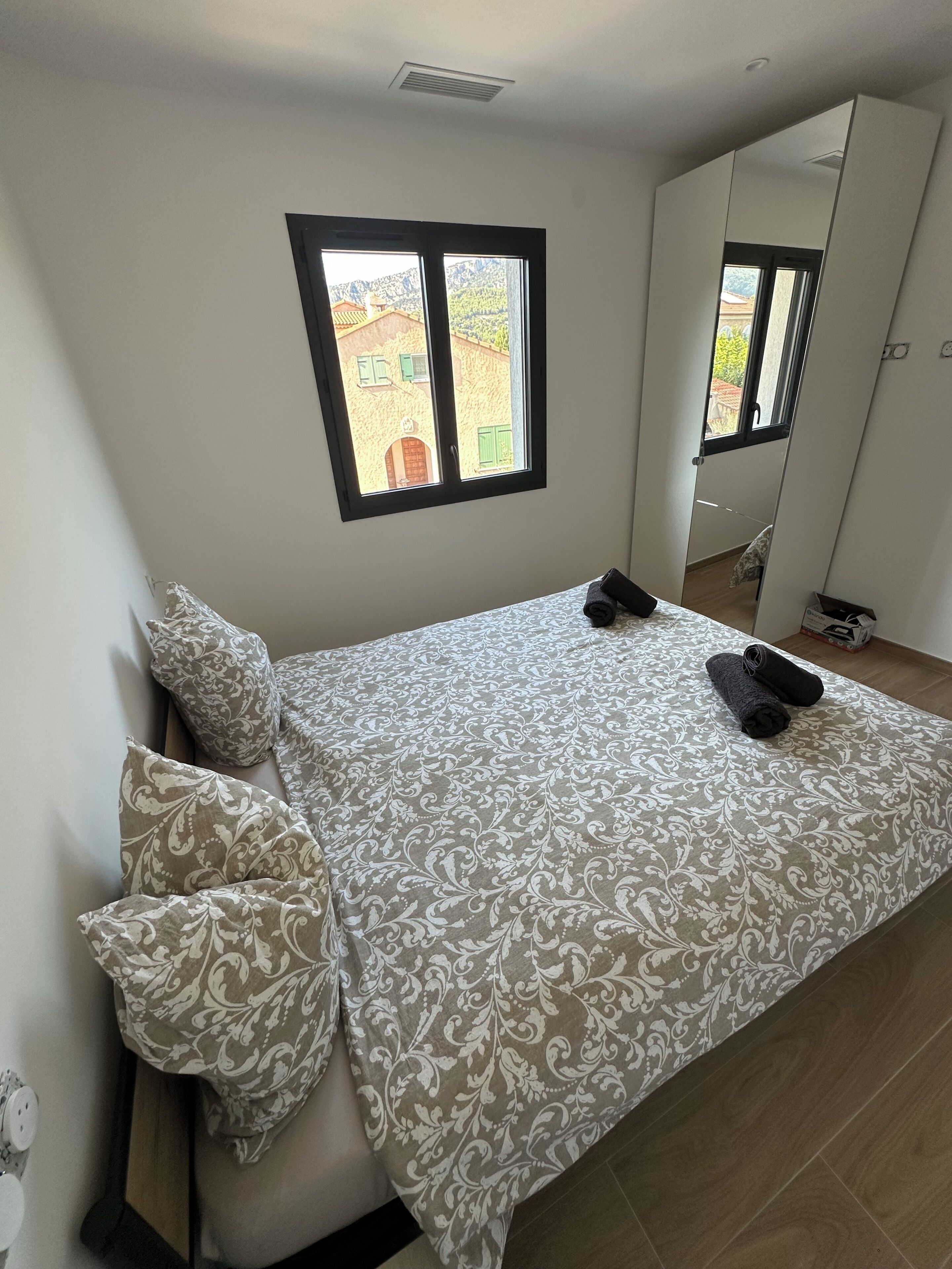 A bedroom with a bed, pillows, a window, a mirror, and a wardrobe.