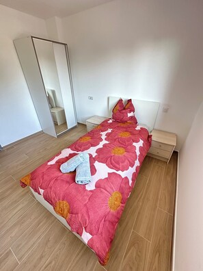 Un dormitorio con cama, mesita de noche, cómoda, espejo y puerta.