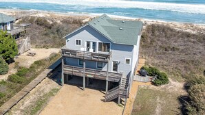 A two-story beachfront house with a balcony, a deck, and a sandy yard. - Making Memories: Oceanfront 6 BR | Hot Tub | Shared Pool (Duck)