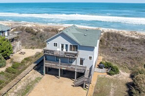 Ein zweistöckiges Strandhaus mit Balkon, Terrasse und einem Sandhof.