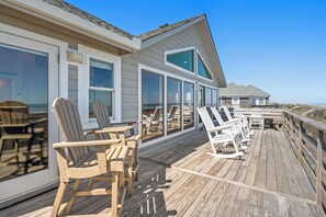 A wooden deck with outdoor seating and large windows. - Making Memories: Oceanfront 6 BR | Hot Tub | Shared Pool (Duck)