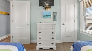 A bedroom with two white doors, a dresser with drawers, a mounted TV, and a window with blinds. - Making Memories: Oceanfront 6 BR | Hot Tub | Shared Pool (Duck)