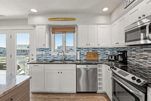 A modern kitchen with white cabinets, a stainless steel dishwasher, a built-in oven, and a microwave. - Making Memories: Oceanfront 6 BR | Hot Tub | Shared Pool (Duck)