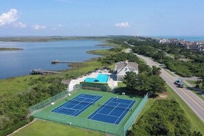 An aerial view of a residential area with a tennis court, a swimming pool, and a dock extending into a body of water. - Making Memories: Oceanfront 6 BR | Hot Tub | Shared Pool (Duck)