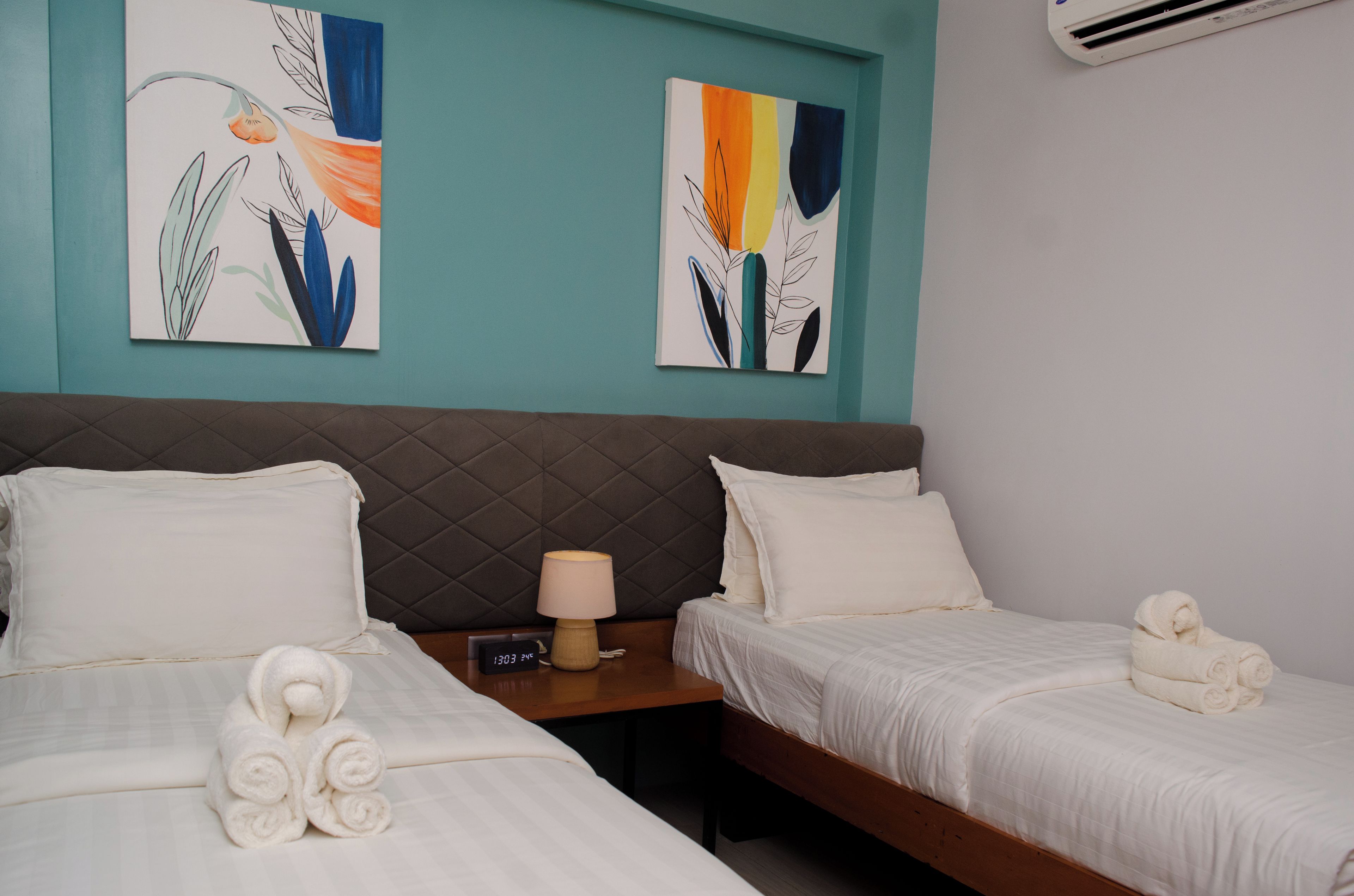 A hotel room with two beds, a nightstand, a lamp, and two wall art pieces.