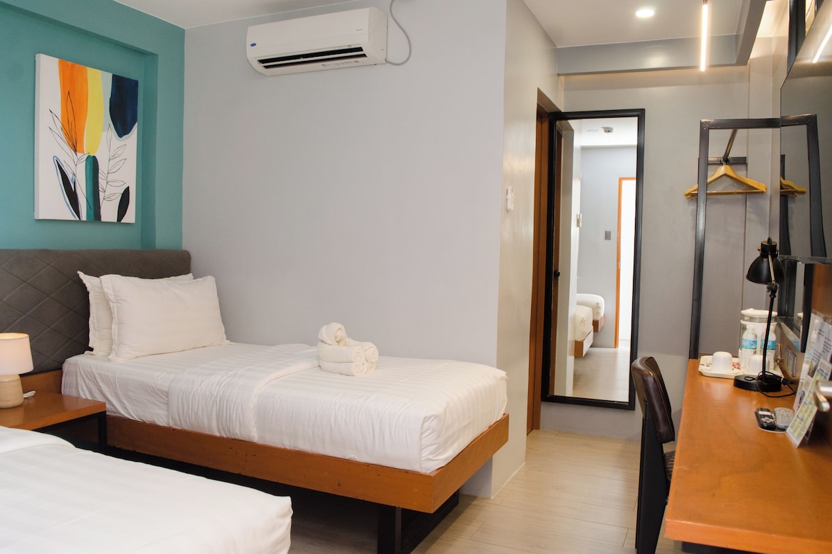 Una habitación de hotel con cama, mesita de noche, lámpara, aire acondicionado y espejo.
