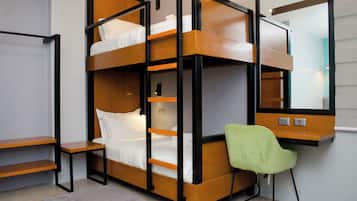 Una cama individual superpuesta con escritorio, silla, espejo y un interruptor de luz en la pared.