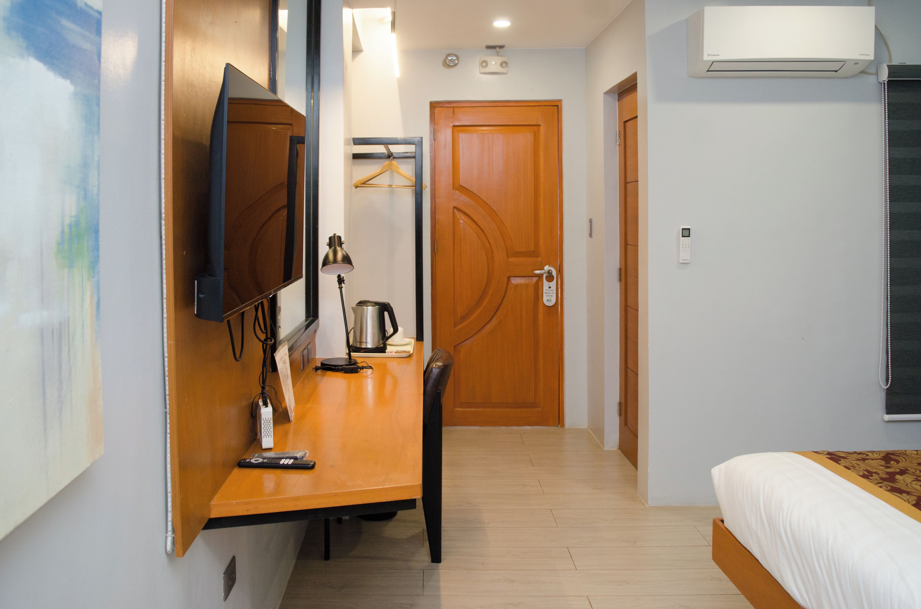 Habitación de hotel con cama, escritorio con silla, televisor, cafetera y puerta con manija.