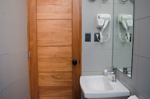 A bathroom with a wooden door, a white sink, a mirror, and two hair dryers mounted on the wall.
