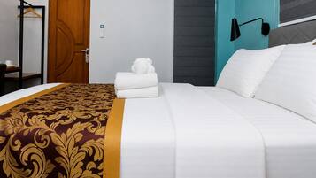 Habitación de hotel con cama, puerta de madera, perchero y una lámpara fijada a la pared.