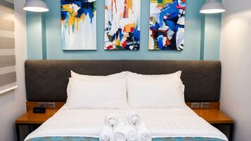 Een hotelkamer met een bed, twee nachtkastjes, een hoofdeinde en drie abstracte schilderijen aan de muur.