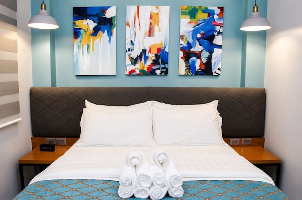 A hotel room with a bed, two bedside tables, a headboard, and three abstract paintings on the wall.