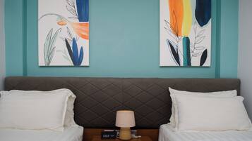 Habitación de hotel con cama, dos almohadas blancas, mesita de noche con lámpara y dos cuadros abstractos en la pared.
