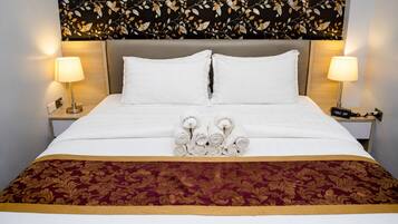Habitación de hotel con una cama, dos lámparas de noche, un reloj digital y una pared decorativa con un diseño de hojas.