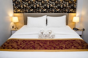 A hotel room with a bed, two bedside lamps, a digital clock, and a decorative wall with a leaf pattern.