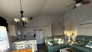 Una cucina moderna con mobili bianchi, un'area pranzo con tavolo in legno e sedie bianche, un divano verde e una ventola a soffitto.