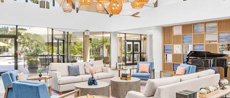 A spacious lobby with seating areas, a grand piano, and large windows offering views of the outdoors.