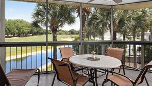 Ein überdachter Außenbereich mit Tisch und Stühlen, mit Blick auf einen Golfplatz und ein Gewässer.