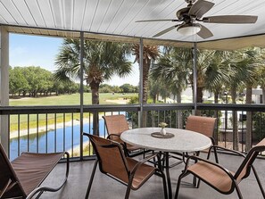 Ein überdachter Außenbereich mit Tisch und Stühlen, mit Blick auf einen Golfplatz und ein Gewässer.